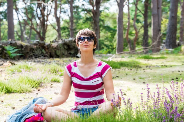 A woman meditating after hiking in the summer forest. Enjoy the sun on the meadow with flowers. Unity with nature, digital detox, personal fulfillment, calm, and harmony. Local traveling in spring