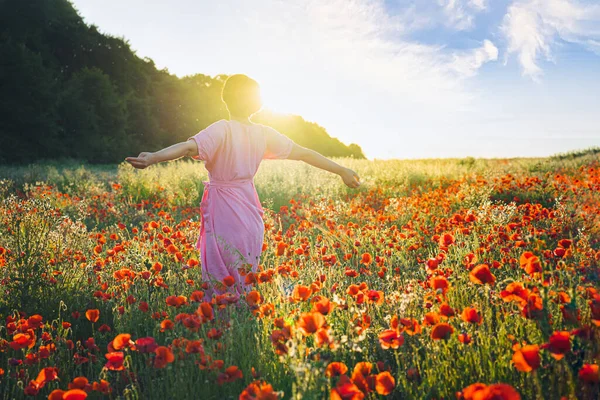 Vista previa mujer joven feliz en un vestido rosa con los brazos levantados relajante en flores de amapolas rojas prado en la luz del atardecer. Un simple placer para la salud mental. Naturaleza relajación. Enfoque selectivo. Copiar espacio —  Fotos de Stock