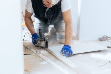 Tamir işlerinde fayans kesme ekipmanlarıyla çalışan inşaat işçilerini kapatın. DIY, kendin yap. Ev tadilatı. Seçici odak, boşluğu kopyala