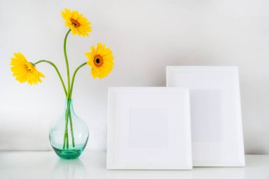 Masadaki cam vazoda sarı Gerbera çiçekleri olan iki boş tahta çerçeve modeli. Poster ürün tasarımı modeli. Çerçeve düzeni. Minimalist ev dekorasyonu. Seçici odaklanma. Boşluğu kopyala.