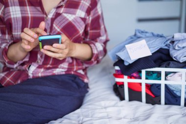 Elbiselerini bağışlayacağı bir yer bulmak için akıllı telefonunu kullanan kadını kapat. Giysileri düzenlemek, sıralamak ve temizlemek. Bilinçli tüketici, sürdürülebilirlik. Tekrar kullan, ikinci el, Charity konsepti.