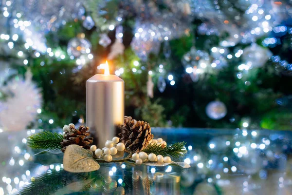 Серебряная горящая свеча с рождественским декором ели и конусов, перед зеленой елкой с боке огни, избирательный фокус, копировальное пространство. — стоковое фото