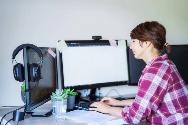 Mulher vista lateral trabalhando no PC com poucos monitores no espaço de trabalho em casa. Conceito de trabalho remoto. Espaço de trabalho freelancer. Foco seletivo. Espaço de cópia. — Fotografia de Stock