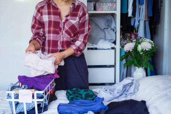 A Woman selecting clothes from her wardrobe for donating to a Charity shop. Decluttering Clothes, Sorting, And Cleaning Up. Reuse, second-hand concept. Conscious consumer, sustainable lifestyle. — Stock Photo, Image