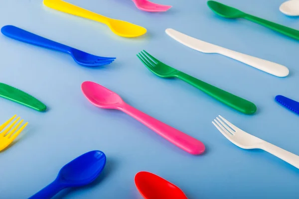 The pattern of reusable cutlery on the blue background. Plastic spoons, forks, knives. Summer Picnic. Plastic recycle concept.