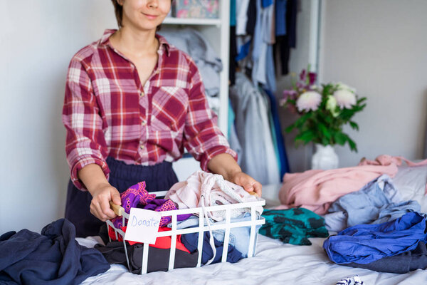 A Woman with selected clothes from her wardrobe for donating to a Charity shop. Woman Decluttering Clothes, Sorting, And Cleaning Up. Reuse, second-hand concept. Conscious consumer, sustainability.