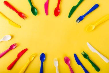 Sarı arka planda yeniden kullanılabilir çatal bıçak takımından yapılmış oval çerçeve. Plastik kaşıklar, çatallar, bıçaklar. Yaz pikniği. Plastik geri dönüşüm kavramı.