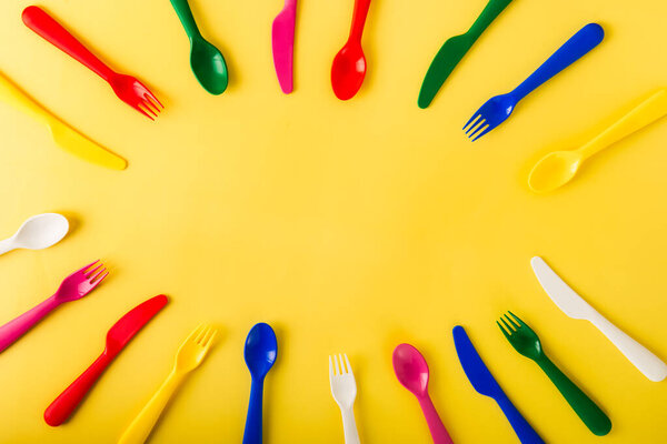 Oval frame made of reusable cutlery on the yellow background. Plastic spoons, forks, knives top view. Summer Picnic. Plastic recycle concept.