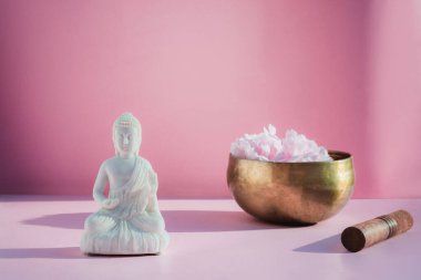 Dekoratif beyaz Buda heykelciği ve pembe arka planda Tibet şarkı kasesi. Meditasyon ve rahatlama ayini. Egzotik masaj. Minimalizm. Doğrudan güneş ışığı ve gölgeler. Uzayı kopyala. Seçici odak