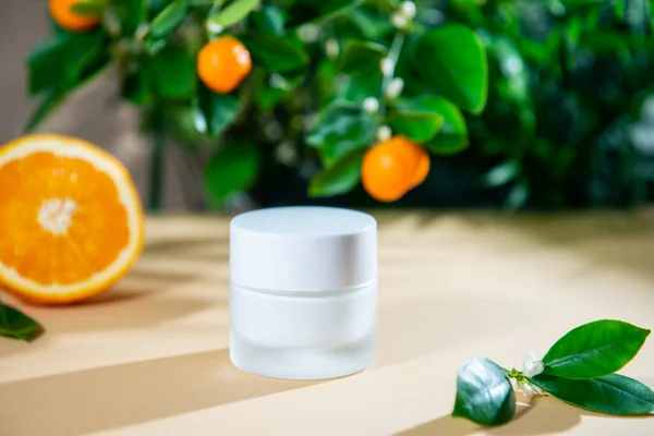 Close up closed jar of moisturizing face cream with natural citrus essential oil and tangerine tree and orange fruits background. Mockup for skin care beauty product. Vitamin C cosmetics. Copy space. — Stock Photo, Image