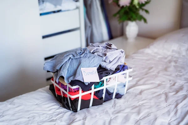 Un panier de vêtements sélectionnés pour faire un don à un magasin de charité debout sur le lit. Déshabiller les vêtements, trier et nettoyer. Réutilisation, d'occasion. Consommateur conscient, durabilité. — Photo