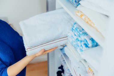 Kadın elleri havluları tutuyor ve modern depolama sisteminin temizlik sırasında gardırop çekmecesindeki bir rafa koyuyor. Rahat ev-uzay organizasyonu kavramı. Seçici odak