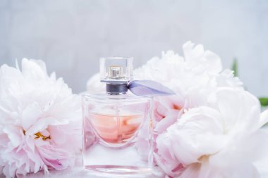 Etrafında büyük açık pembe şakayık çiçekleri olan narin bir çiçek parfümü şişesi. Kopyalama alanı olan bir model. Seçici odak.