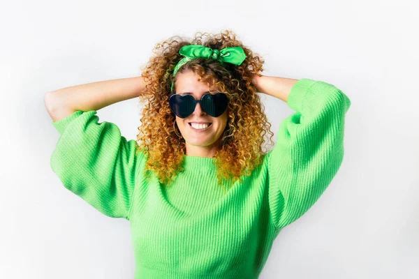 Retrato de mulher sorridente feliz em um pulôver verde brilhante e óculos de sol em forma de coração no fundo branco. Amor, emoções expressas, conceito de expressão facial positiva. Espaço de cópia — Fotografia de Stock