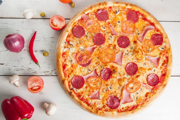 Close up Delicious Meat Pizza with Salami, Bacon and Tomato Slices on a cutting board on white wooden background with different colourful vegetables top view — Stock Photo, Image