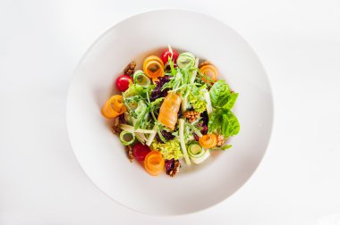 Isolated Delicios Salad with salmon, mix lettuce, arugula, cucumber, walnuts, cherry tomatoes garnished with a sprig of basil on a white plate
