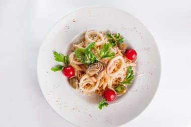 Close up Seafood Salad with squid, mussels, parmesan cheese, lettuce, mix olives, arugula, tomatoes, decorated with a sprig of basil on white plate isolated on white background