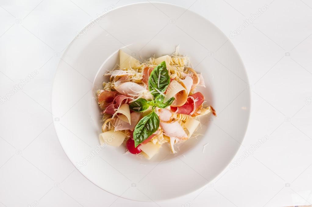 Top view Close up  Plate of meat Pasta with ham and  prosciutto slices decoratred with cherry tomatos, parmesan cheese and basil on the white plate isolated