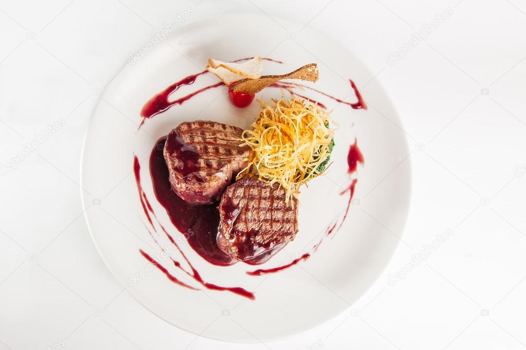 Restaurant serves meat steak with spinach pillow and potato's brushwood in berry sauce, garnished with breadcrumbs and cherry tomatoes on white plate isolated
