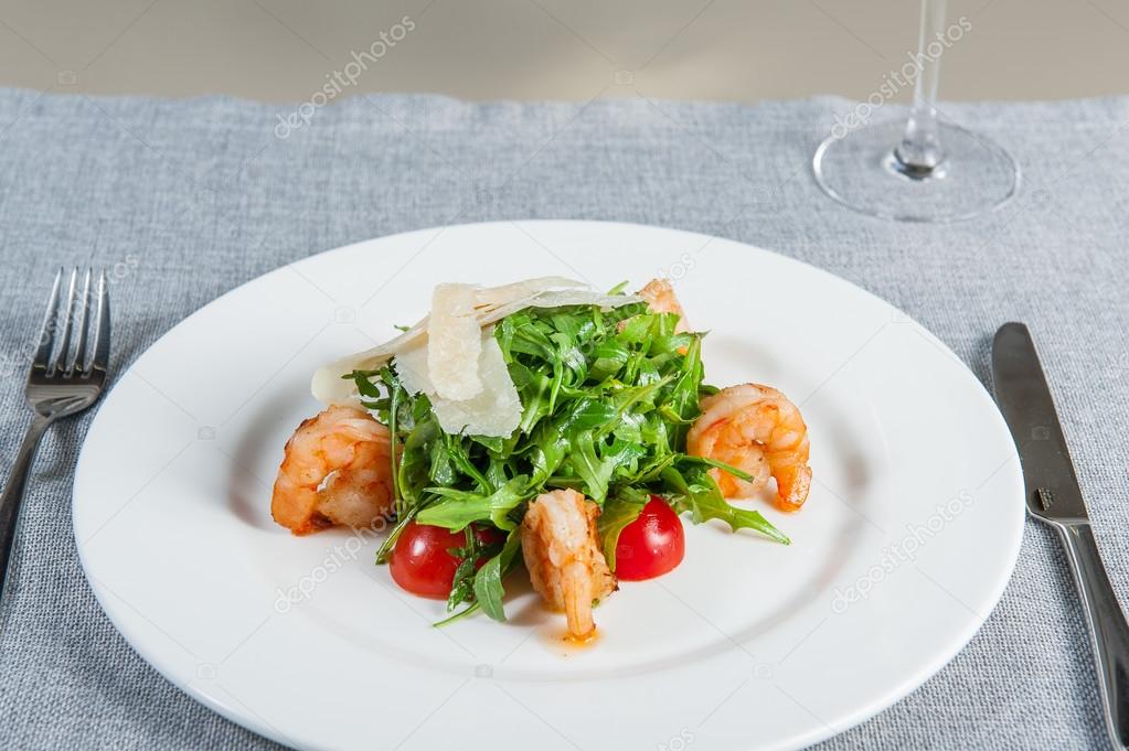 Delicious salad with shrimps, arugula, cherry tomatoes and Parmesan cheese, seasoned with balsamic sauce on served for dinner restaurant table