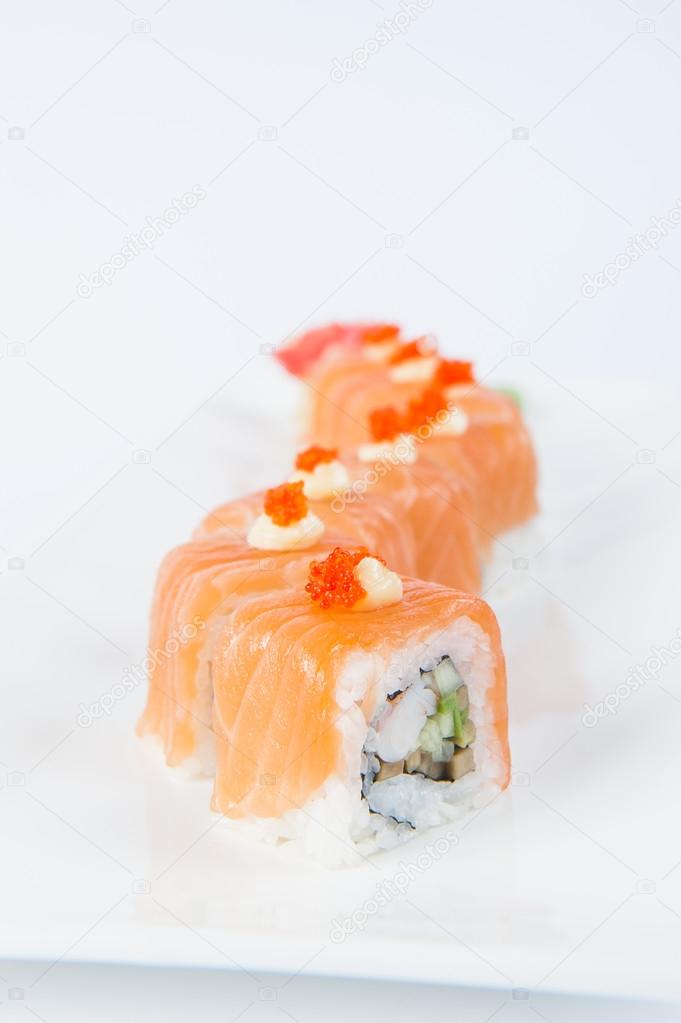 Traditional fresh japanese Salmon sushi rolls with shrimps, avocado and cucumber inside decorated with Red caviar on white plate isolated on a white background