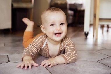 Happy, laughing baby lying on tiled floor at home for child development, wellness and growth. Cheerful active little infant kid training physical skills, smiling, learning to crawl, playing and relax