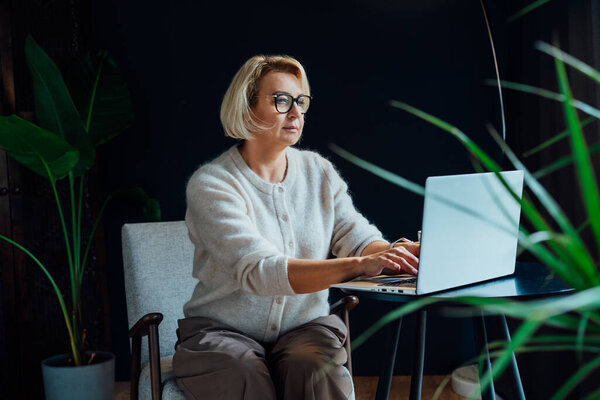 Smiling 50s stylish, confident mature businesswoman, middle aged experienced senior female professional, business coach, mentor, therapist, counselor working on laptop in office. Female leader.
