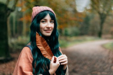 Sıcak şallı Ponço giymiş genç bir kadın düşen yaprağı tutuyor ve sonbahar orman yürüyüşünde huzur ve özgürlüğün tadını çıkarıyor. Ahengi hissetmek, doğayla bir araya gelmek. Rahatlatıcı, zihinsel iyileşme