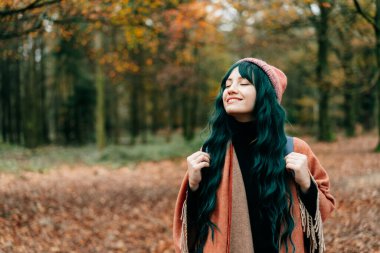 Sıcak şallı, şallı, gözleri kapalı gülümseyen kadın sonbahar ormanında sarı yapraklarla huzur ve özgürlüğün tadını çıkarıyor. Ahengi hissetmek, doğayla bir araya gelmek. Rahatlatıcı, zihinsel iyileşme