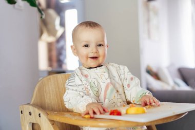 Gülümseyen sevimli bebek kendini yüksek sandalyede yiyor bebek sütten kesilmesine ya da kızarmasına neden oluyor. Bebek kendini besleyen katı besinler, iyi motor geliştirme. Bebekler tek başına beslenir, öğrenir, yemek yer ve ortalığı dağıtır..