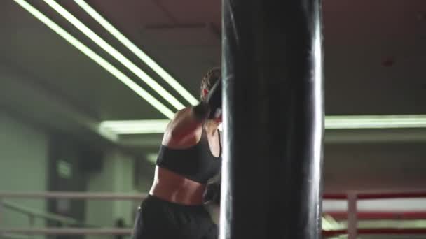 Boxe, mulher lutadora treina seus socos, bate um saco de perfuração, dia de treinamento no ginásio de boxe, corpo de ajuste de força, a menina bate rápido. — Vídeo de Stock