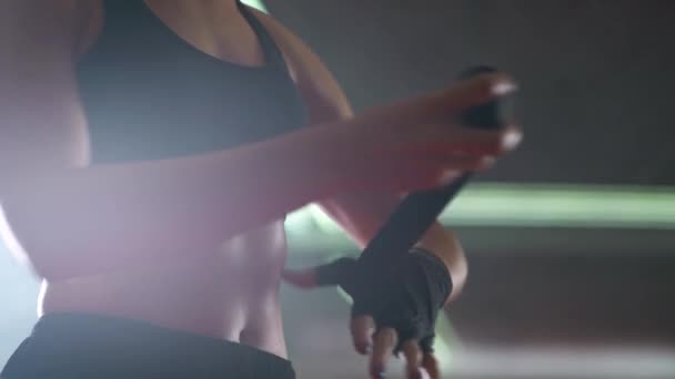 Combattant femme enveloppe ses mains avec des bandages de boxe, journée d'entraînement de kickboxing dans une salle de gym, éclairage au néon. — Video