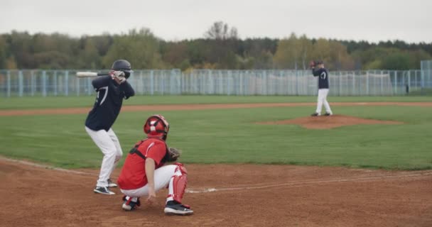 Vysokoškolské sporty, kluci hrají baseball, nadhazovač hodí míč směrem k pálce, pálkař úspěšně trefí rychlý míč, 4k 50fps. — Stock video