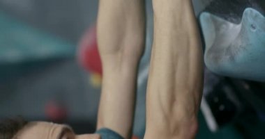 Genç adam dik bir duvara tırmanıyor, bir tırmanma duvarında antrenman yapıyor, kaya tırmanışı yapıyor, yükseliyor. 4k 50fps.