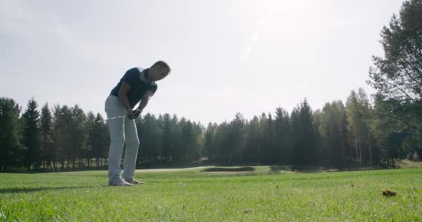 Letni dzień, mężczyzna grający w golfa, uderza piłkę, widok na pole golfowe w lesie, zielony trawnik, 4k zwolnione tempo. — Wideo stockowe