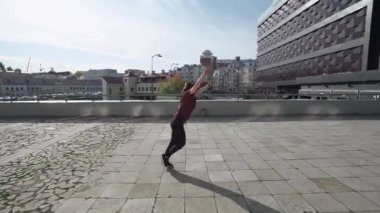 Genç bayan jimnastikçi bir dizi takla atıyor ve modern binaların yakınındaki eğitim alanında koşuyor..