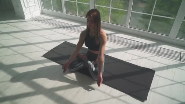 Bienestar, joven mujer medita y hace yoga, un estado de ánimo tranquilo, relajarse en una habitación blanca llena de luz, la chica está sentada en el suelo, movimiento de la cámara. — Vídeos de Stock