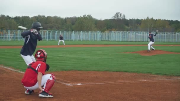 Főiskolai sportok, srácok baseballoznak, a dobó dobja a labdát az ütő felé, az ütő sikeresen eltalálja a gyorslabdát és elfut a bázisra.. — Stock videók