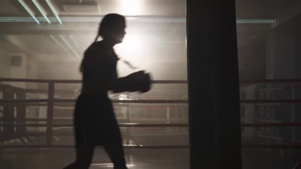 Kickboxing, mulher lutadora treina seus socos, bate um saco de perfuração, dia de treinamento no ginásio de boxe, corpo de ajuste de força, a menina bate rápido. — Vídeo de Stock