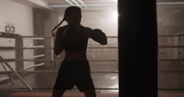 Kadın dövüşçü yumruklarını eğitir, kum torbasını döver, boks salonunda antrenman yapar, arka ışıklandırma yapar..