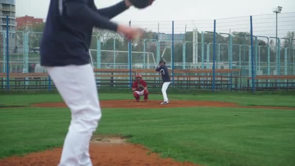 College Sports, faceci grają w baseball, miotacz rzuca piłkę w kierunku pałkarza, pałkarz z powodzeniem uderza szybką piłkę i biegnie do bazy. — Wideo stockowe