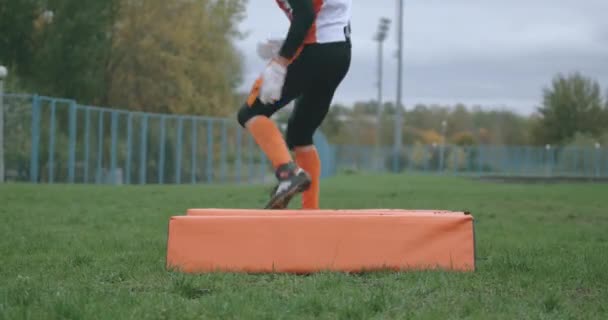 Amerikansk fotboll, ung fotbollsspelare i skyddsutrustning hoppar över hinder, samordningsträning, 4k 50fps. — Stockvideo