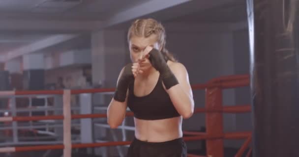 Mujer combate entrena sus golpes, día de entrenamiento en el gimnasio de boxeo, la chica entrena una serie de golpes y mira a la cámara. — Vídeos de Stock