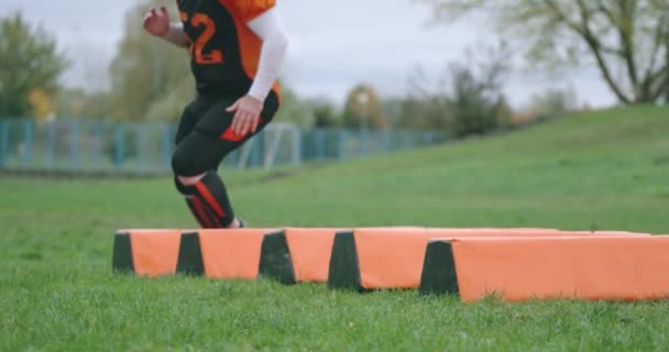 Amerikansk fotboll, ung fotbollsspelare i skyddsutrustning hoppar över hinder, samordningsträning, 4k slow motion. — Stockvideo