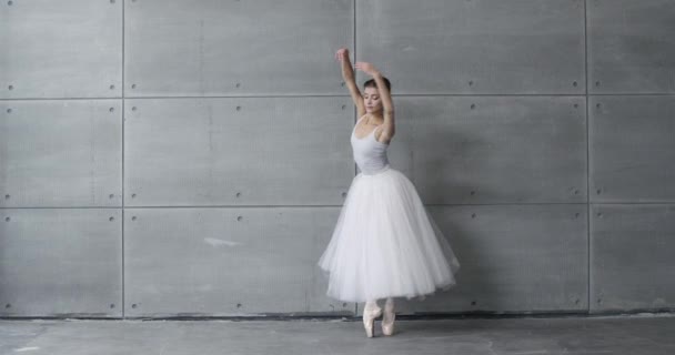 Elegante hembra en un tutú blanco, baila ballet y realiza elementos coreográficos sobre un fondo gris, ensayo. — Vídeo de stock