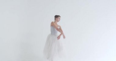 Beyaz etekli zarif bir kadın, bale yapıyor ve beyaz arka planda koreografik elementler sergiliyor..