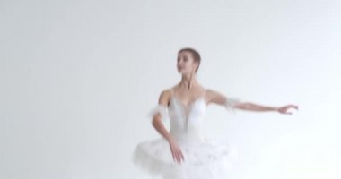 Beyaz etekli zarif bir kadın, bale yapıyor ve beyaz arka planda koreografik elementler sergiliyor..