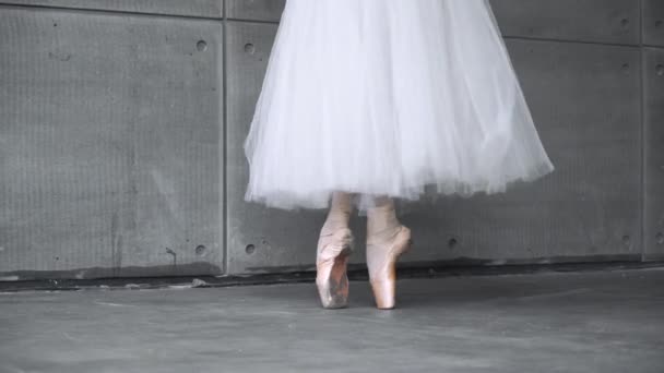 Elegante hembra en un tutú blanco, danza ballet y equilibrio en zapatos de punta, vista de las piernas, fondo gris, ensayo. — Vídeos de Stock