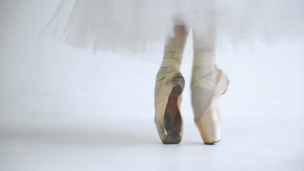 Vrouw in een witte tutu, dansballet en balancering in Pointe schoenen, blik op de benen, witte achtergrond, repetitie. — Stockvideo