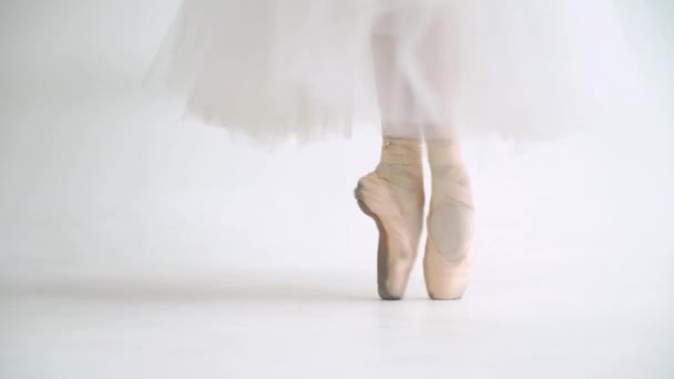 Vrouw in een witte tutu, dans ballet en balanceren in Pointe schoenen, uitzicht op de benen, witte achtergrond. — Stockvideo